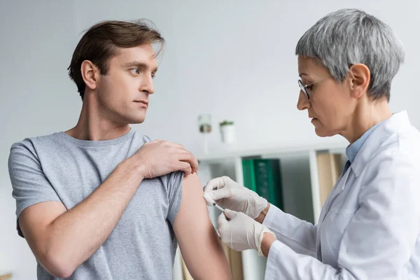 Reife Ärztin impft Mann in Klinik — Stockfoto