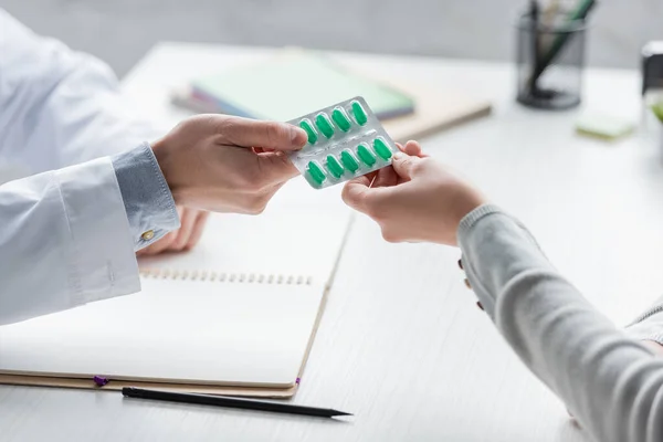 Cropped view of doctor giving blister with pills to woman in clinic — Stock Photo