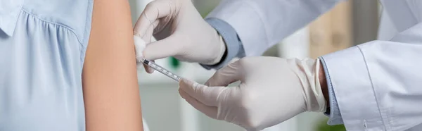 Vista recortada del médico en guantes de látex haciendo la vacunación de la mujer, bandera - foto de stock