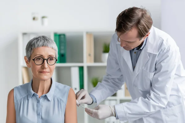 Patient mittleren Alters sitzt in Latexhandschuhen neben Arzt bei Impfungen — Stockfoto