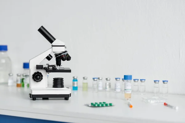 Microscope near vaccines and syringes on blurred foreground in laboratory — Stock Photo