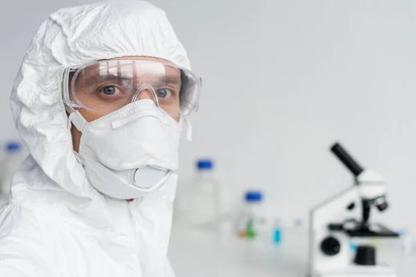 Scientist in goggles and hazmat suit looking at camera in laboratory — Stock Photo