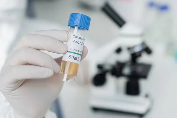Cropped view of scientist in latex glove holding coronavirus vaccine in laboratory — Stock Photo
