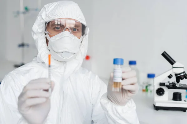 Scientist holding syringe and vaccine on blurred foreground in laboratory — Stock Photo