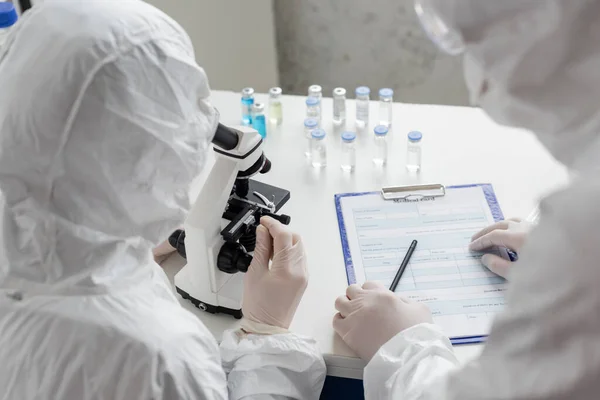Scientists working with clipboard and microscope near vaccines — Stock Photo