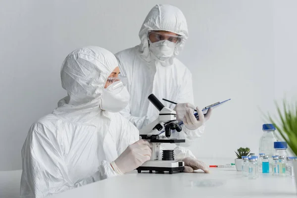 Вчений використовує мікроскоп поблизу колеги з буфера і вакцинами — стокове фото