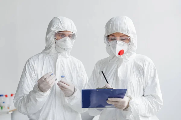 Scientists in hazmat suits working with vaccines and clipboard in laboratory — Stock Photo