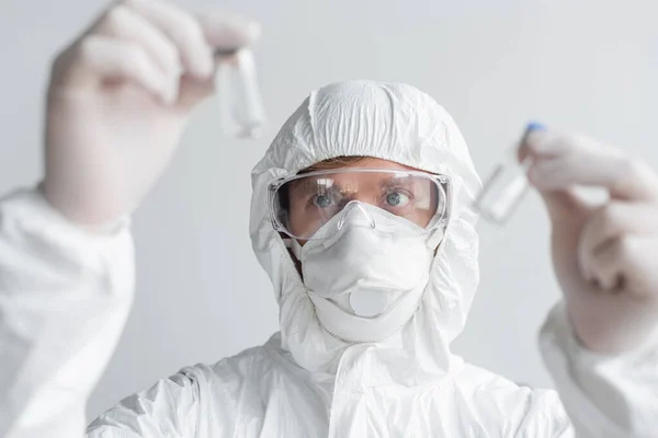 Вчений у костюмі з туманом дивиться на вакцини на розмитому передньому плані — стокове фото