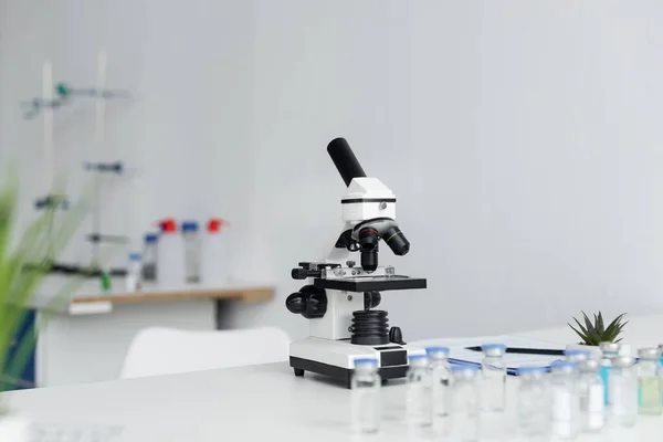Microscope and vaccines on blurred foreground in laboratory — Stock Photo