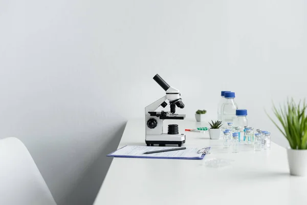 Microscope near vaccines and clipboard on table in laboratory — Stock Photo