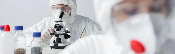 Вчений, який працює з мікроскопом біля колеги на розмитому фоні, банер — стокове фото