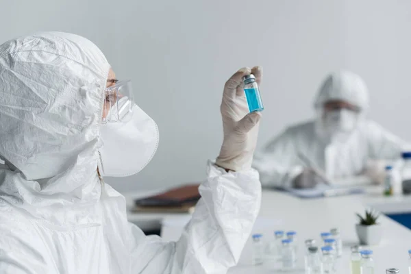 Científico mirando frasco con vacuna cerca colega en fondo borroso - foto de stock
