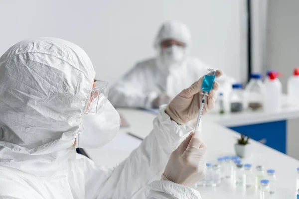 Вчений збирає вакцину в шприці біля колеги на розмитому фоні — стокове фото