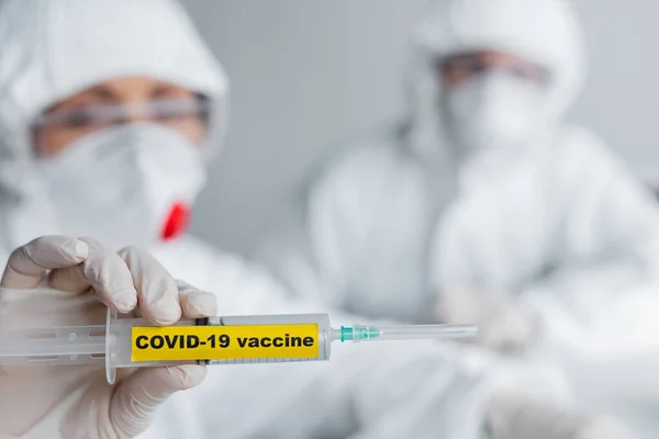 Syringe with covid-19 vaccine lettering in hand of scientist on blurred background — Stock Photo