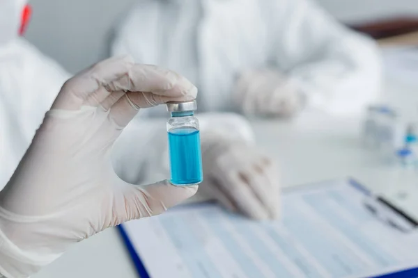 Cropped view of vaccine in hand of scientist on blurred background — Stock Photo