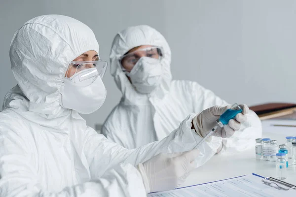 Вчений збирає вакцину в шприці біля буфера обміну та колеги на розмитому фоні — стокове фото