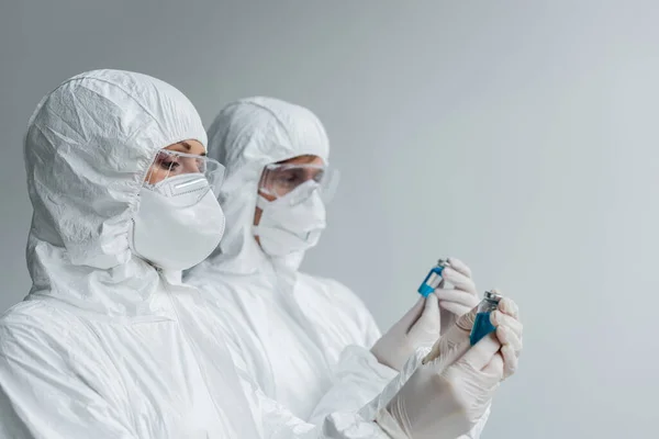 Scientist in hazmat suit and goggles holding vaccine near colleague — Stock Photo
