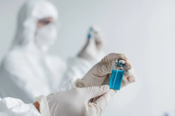 Scientist in latex gloves holding vaccine near colleague on blurred background — Stock Photo