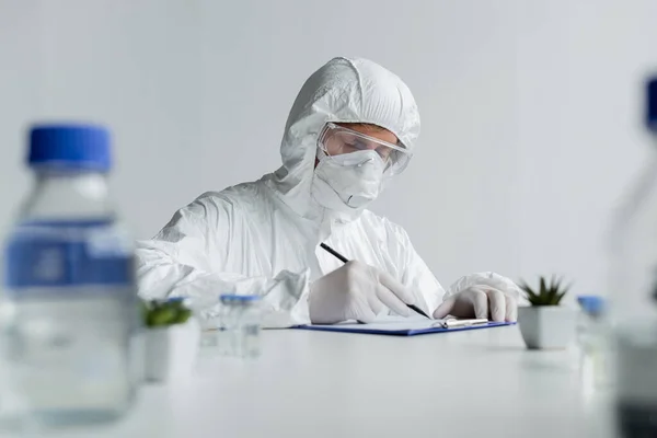 Вчений пише на кишені біля вакцин і рослин на розмитому фоні — стокове фото