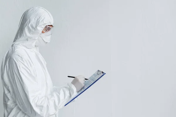 Cientista em uniforme de proteção escrevendo na área de transferência — Fotografia de Stock