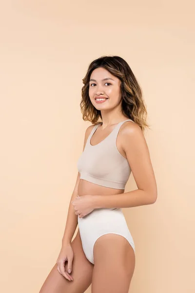 Pleased asian woman in underwear smiling at camera isolated on beige — Stock Photo