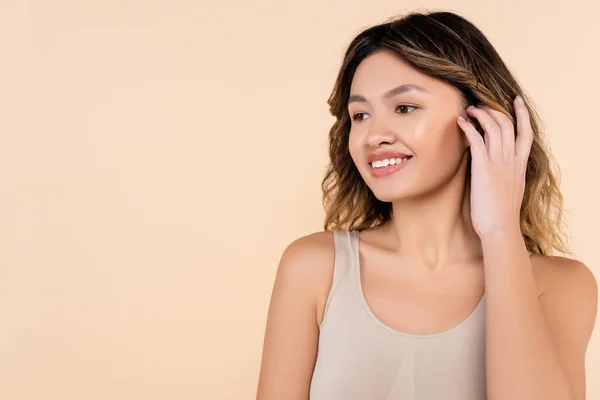 Joven asiático mujer fijación cabello y sonriente aislado en beige - foto de stock