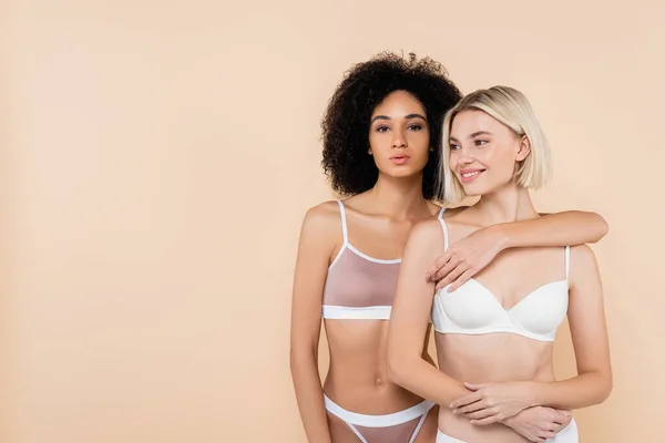 African american woman embracing blonde friend while posing isolated on beige — Stock Photo
