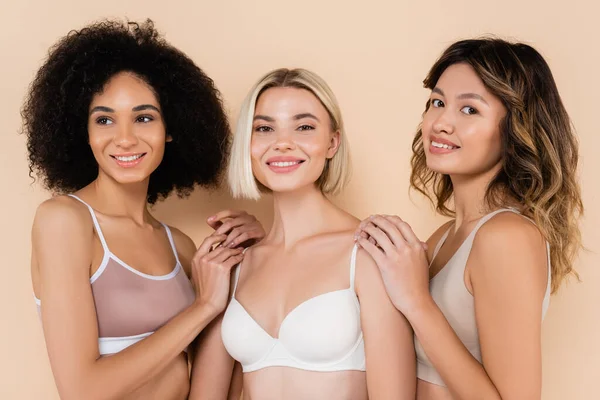 Cheerful multiethnic women in underwear smiling on beige — Stock Photo
