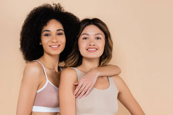 Alegre Africano americano mulher abraçando sorridente asiático amigo isolado no bege — Fotografia de Stock