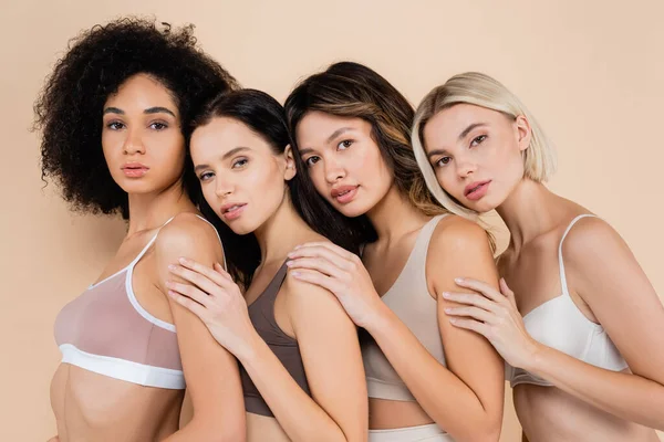 Pretty multiethnic women leaning on each other while looking at camera on beige — Stock Photo