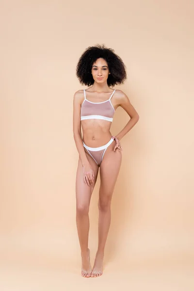 Vue pleine longueur de mince femme afro-américaine en sous-vêtements sur beige — Photo de stock