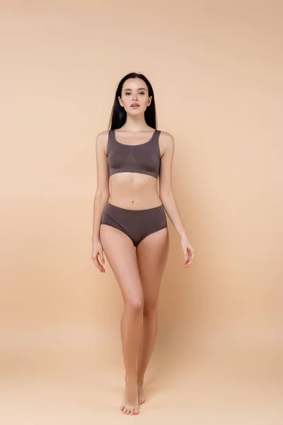 Full length view of young woman in underwear standing on beige — Stock Photo