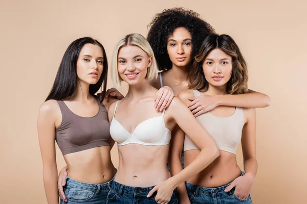 Junge multikulturelle Frauen in BHs und Jeans, die vereinzelt in beige in die Kamera schauen — Stockfoto