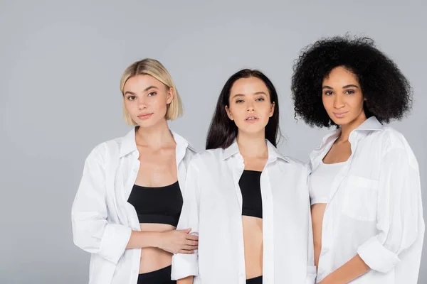 Pretty multiethnic women in white shirts and underwear posing isolated on grey — Stock Photo