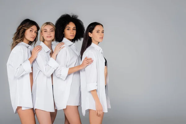 Pretty interracial women in white shirts, with bare legs, posing isolated on grey — Stock Photo