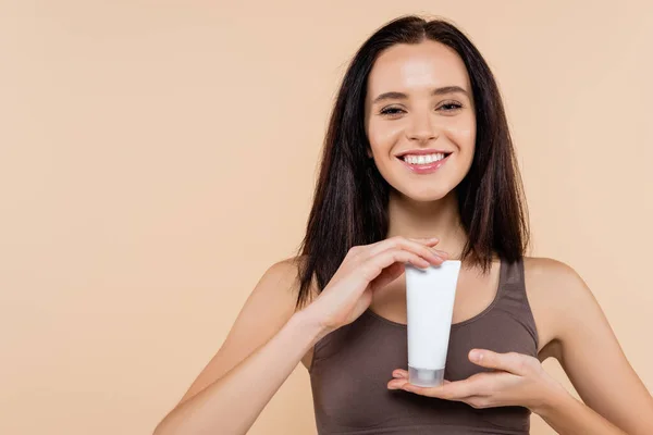 Pleased woman in bra showing cosmetic cream isolated on beige — Stock Photo