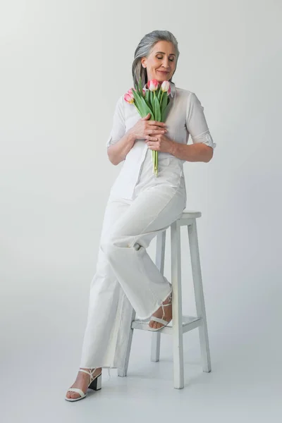 Mujer madura con los ojos cerrados sosteniendo flores sobre fondo gris - foto de stock