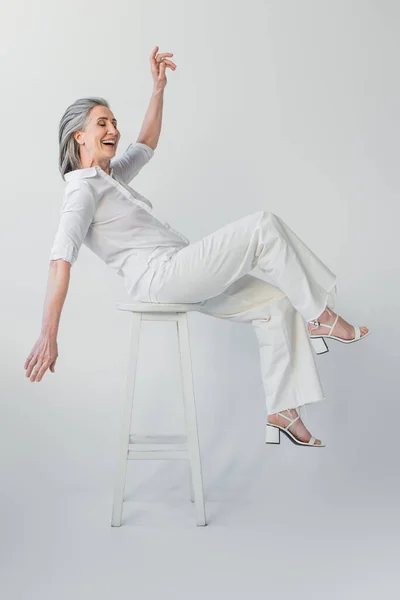 Mujer madura positiva sonriendo en silla sobre fondo gris — Stock Photo