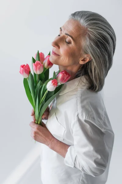 Mature woman holding tulips isolated on grey — Stock Photo