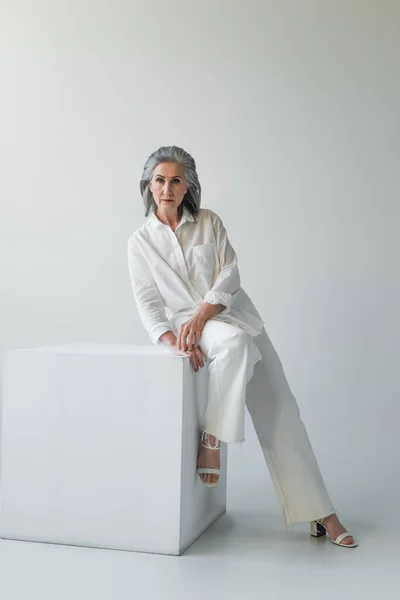 Middle aged woman posing near white cube on grey background — Stock Photo