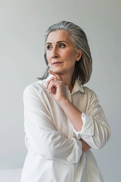 Mature woman with hand near chin posing isolated on grey — Stock Photo