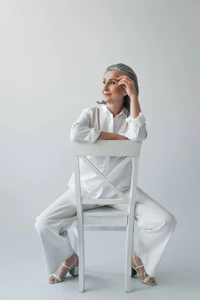 Frau mittleren Alters sitzt auf Stuhl auf grauem Hintergrund — Stockfoto