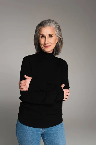 Mature woman in black jumper smiling at camera isolated on grey — Stock Photo