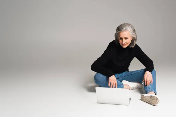 Donna di mezza età che utilizza il computer portatile su sfondo grigio — Stock Photo