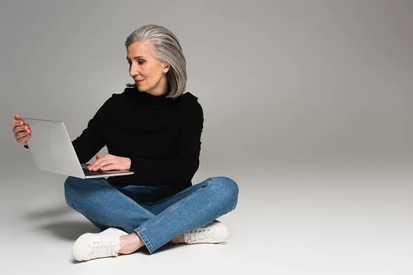 Сіра волохата жінка використовує ноутбук на сірому фоні — стокове фото
