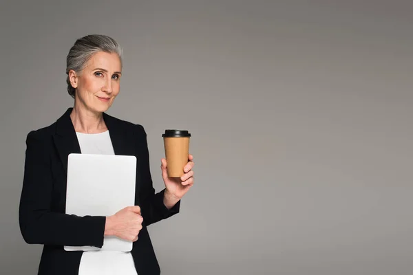 Femme d'affaires d'âge moyen avec café à emporter et ordinateur portable isolé sur gris — Photo de stock