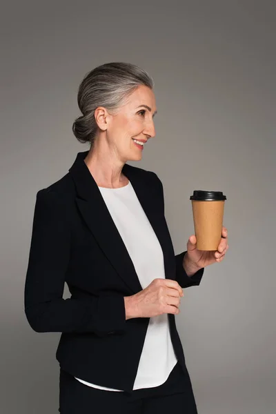 Cheerful businesswoman in formal wear holding takeaway drink isolated on grey — Stock Photo