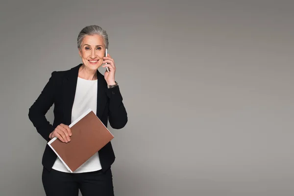 Reifer Manager mit Dokumenten, die auf dem Smartphone sprechen, isoliert auf grau — Stockfoto