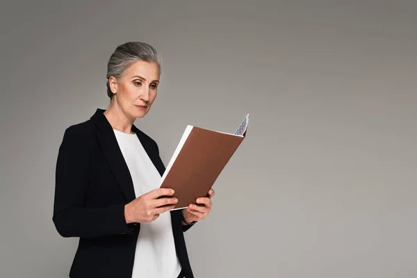 Frau mittleren Alters in formeller Kleidung blickt auf Papiermappe isoliert auf grau — Stockfoto