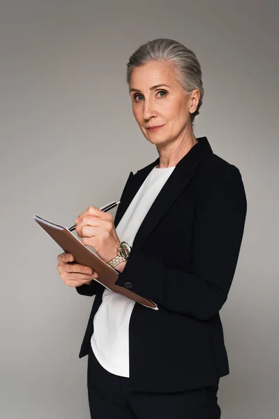 Geschäftsfrau mittleren Alters schreibt auf Papiermappe isoliert auf grau — Stockfoto